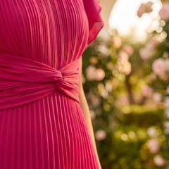 Abito maxi plissettato rosa: cintura annodata e pieghe verticali.