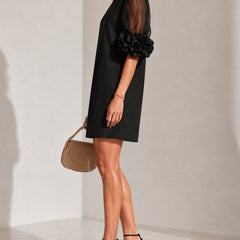 Black puff-sleeve midi dress with sheer sleeve overlay and rosette cuff detail.